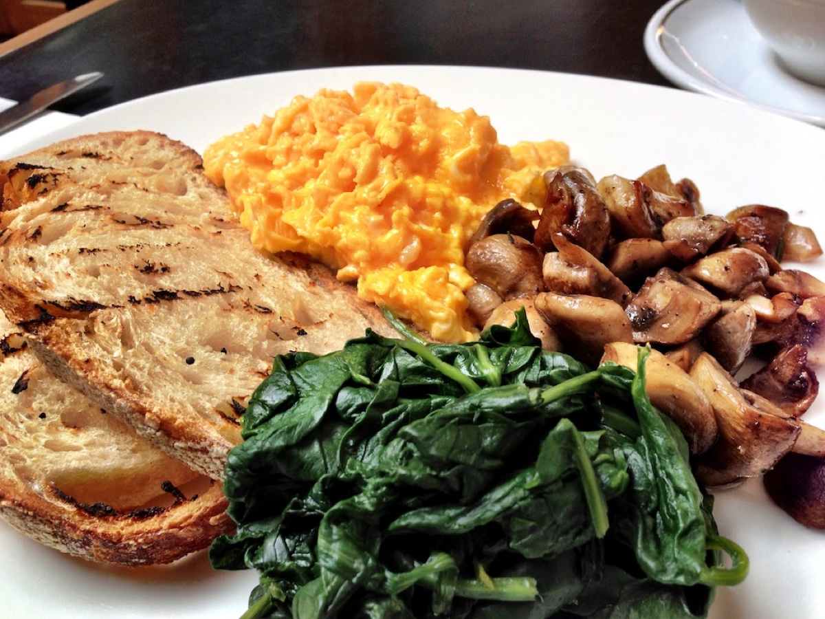 A bowl of soft-scrambled eggs over wilted spinach and kale with a slice of toasted sourdough on the side